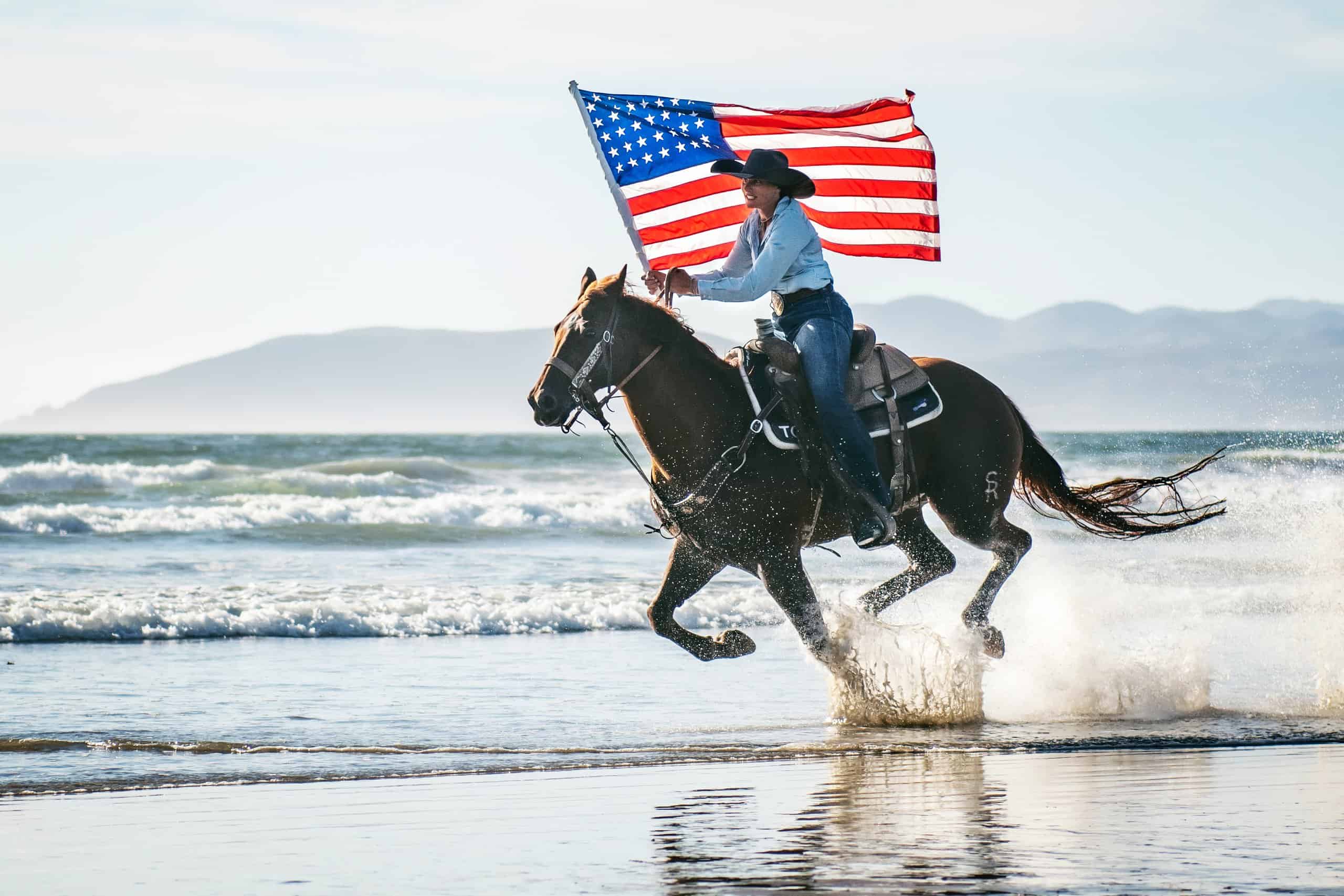 Woman riding horse on beach with USA flag